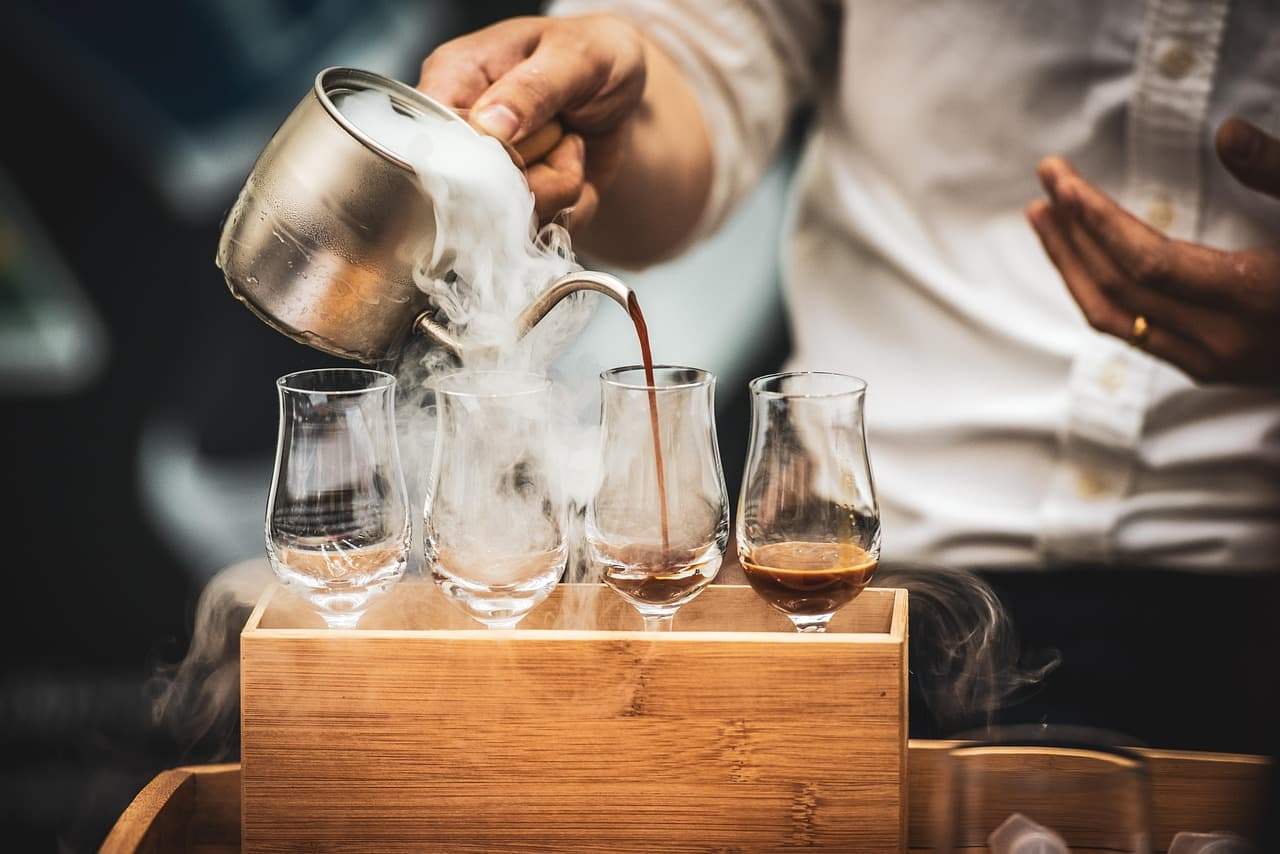 A barista pouring coffee into a row of tasting glasses