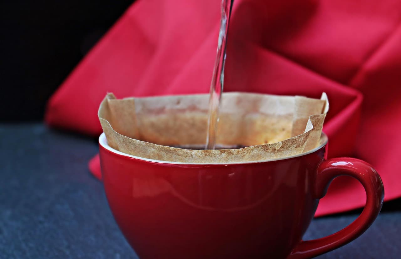 Hot water poured through a paper filter into a red cup