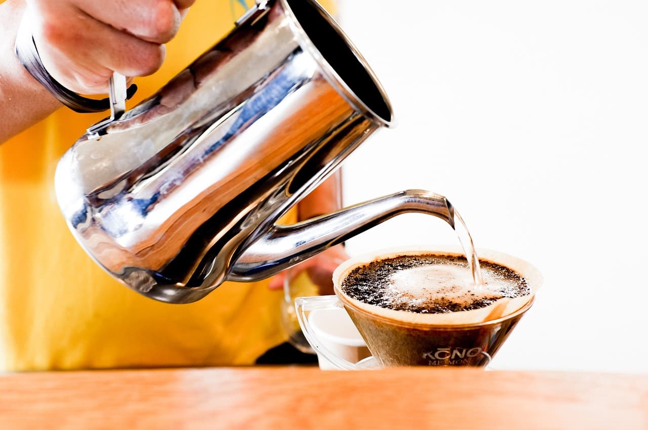 A barista pouring water from a gooseneck kettle over a filter of coffee