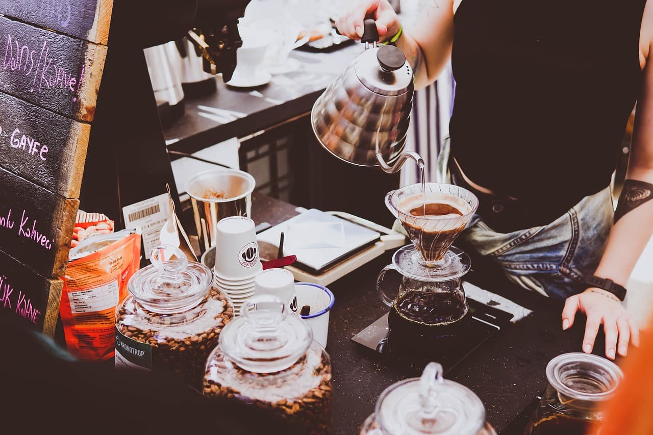 A barista brewing pour-over coffees at a busy bar, kettle in hand